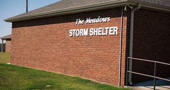 A brick building with a sign that says "The Meadows Storm Shelter".